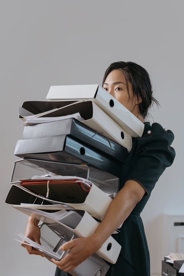 Home Woman carrying a large stack of file folders indoors, expressing stress and workload.