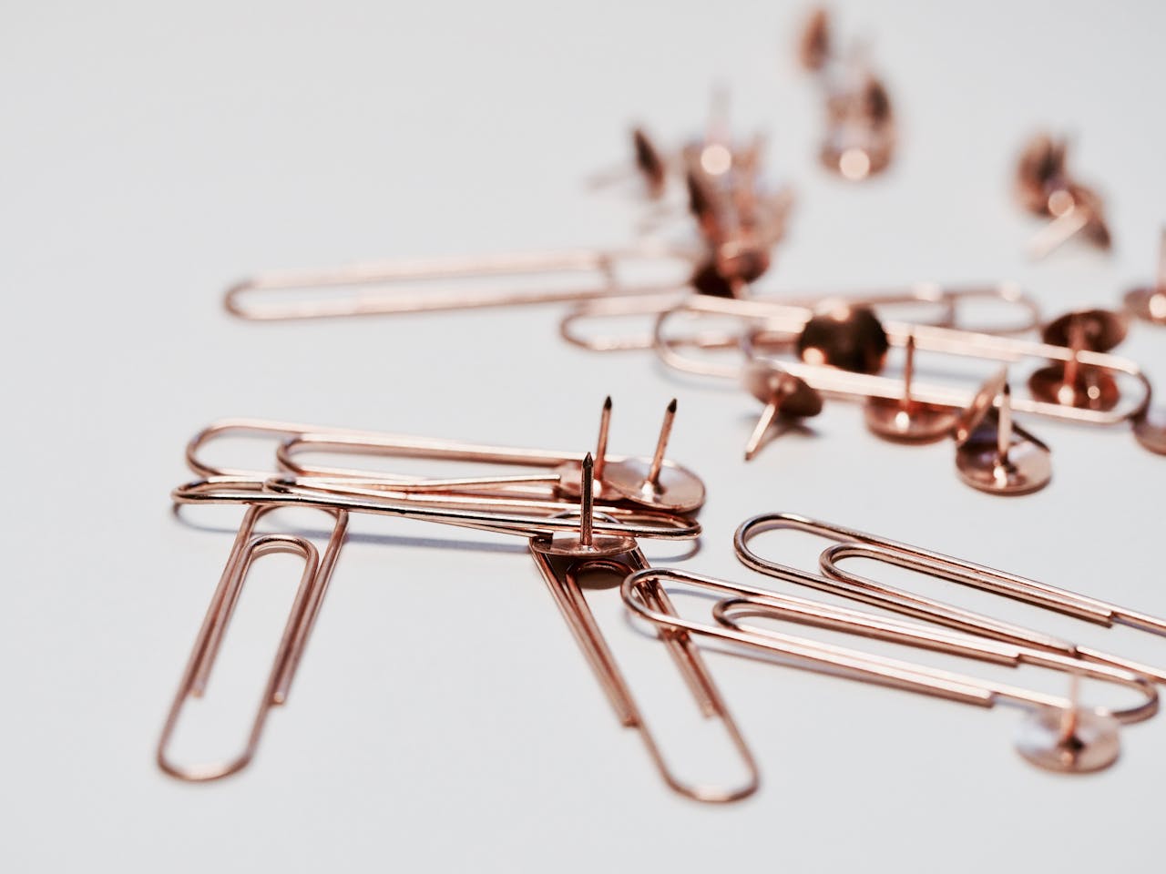 Home Aesthetic rose gold paperclips and thumb tacks on a white background, ideal for office decor or supplies imagery.