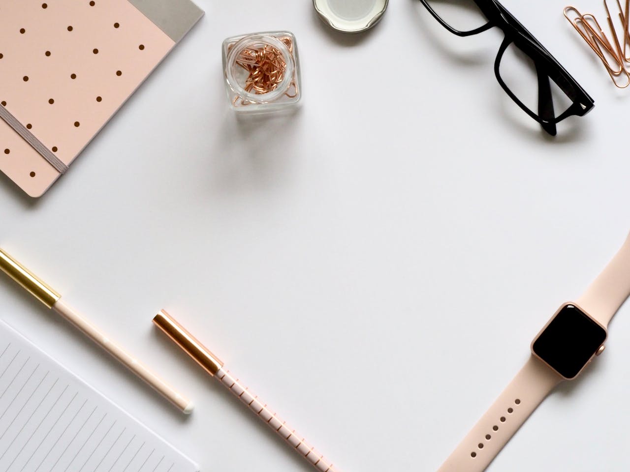 Home Stylish rose gold themed flatlay featuring office supplies and a smartwatch on a white background.