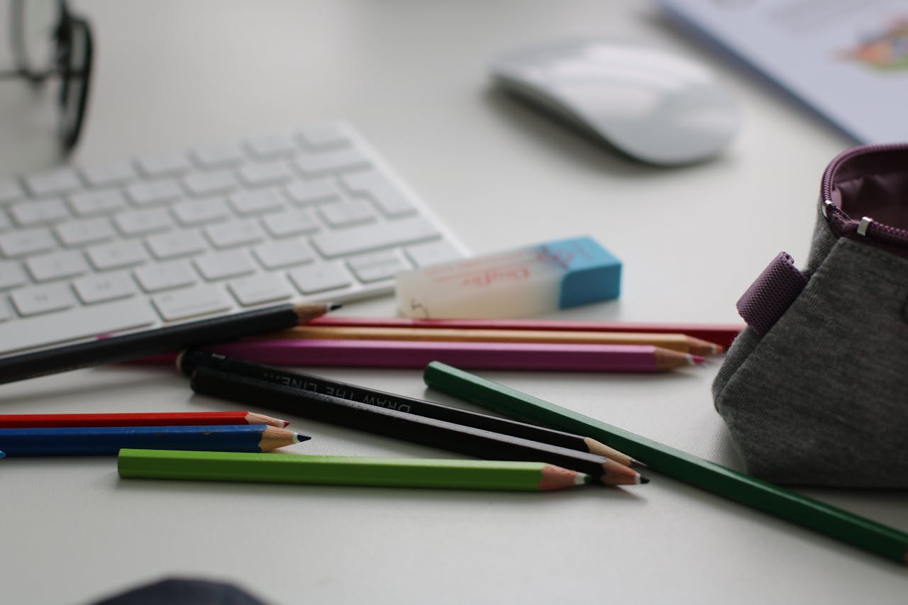 Home Color pencils and office supplies scattered on a white desk with keyboard and mouse.